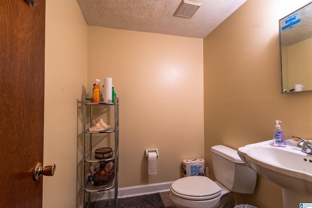 bathroom with baseboards, visible vents, toilet, a textured ceiling, and a sink