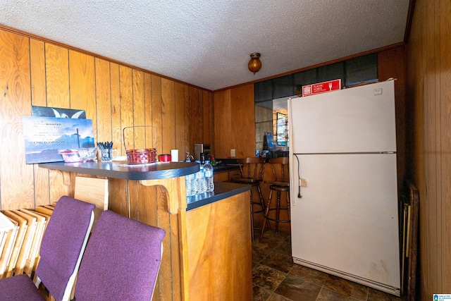 kitchen with dark countertops, wood walls, brown cabinets, and freestanding refrigerator