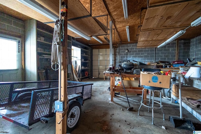 miscellaneous room with a garage, unfinished concrete flooring, and concrete block wall