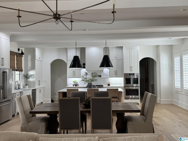 dining area featuring light wood-style flooring, arched walkways, and beamed ceiling