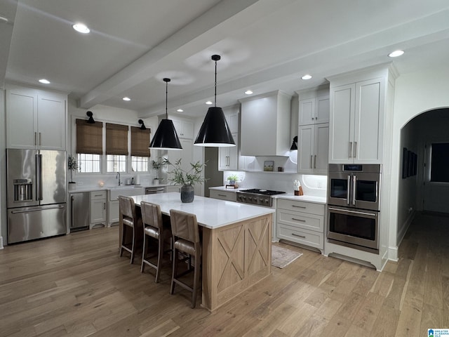 kitchen featuring stainless steel appliances, a kitchen island, light countertops, light wood-type flooring, and beamed ceiling