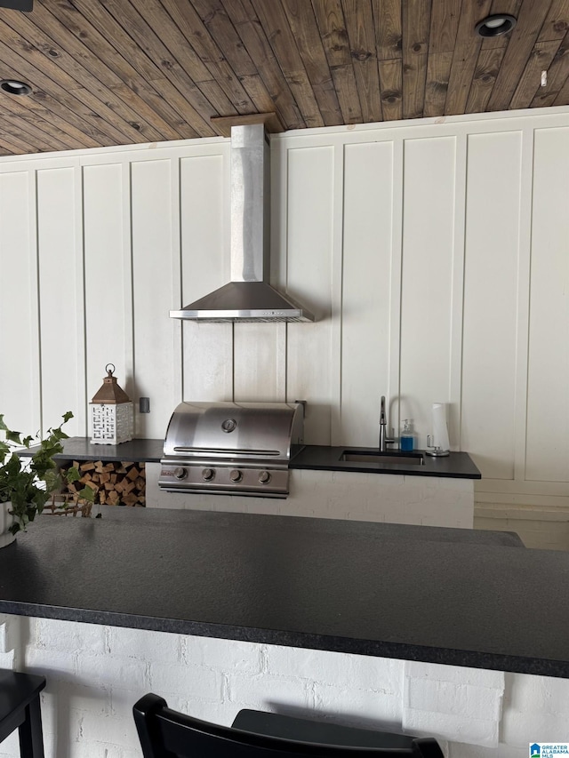 kitchen with white cabinets, wood ceiling, wall chimney exhaust hood, a decorative wall, and a sink