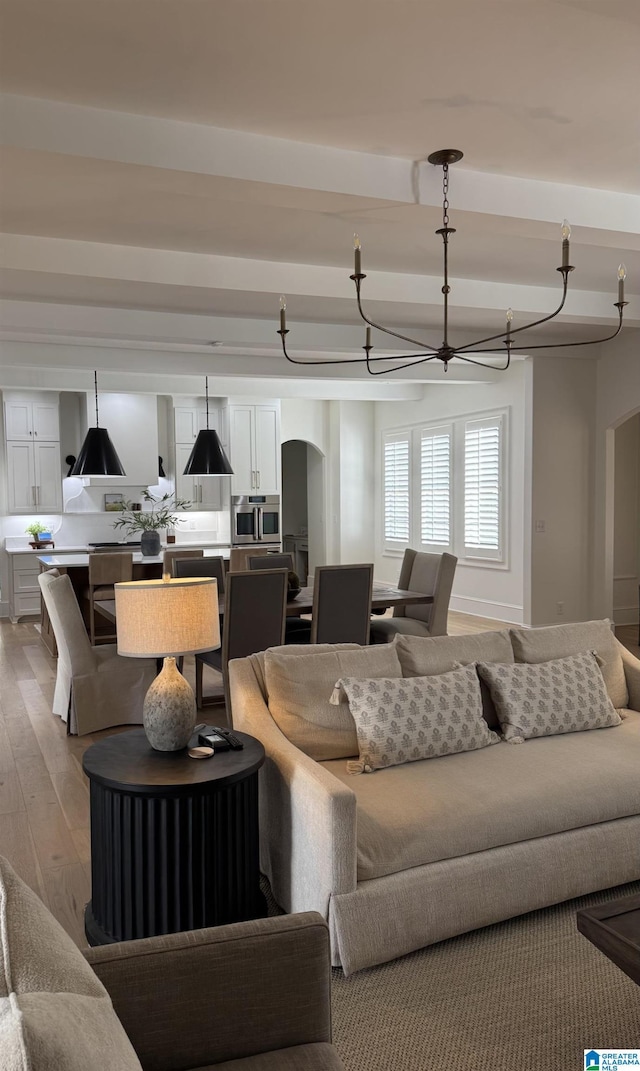 living area with a chandelier, arched walkways, beam ceiling, and wood finished floors