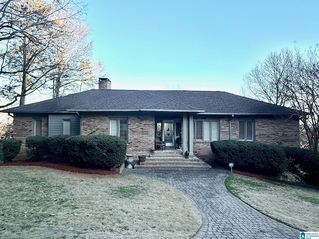 ranch-style home with roof with shingles, a chimney, a front lawn, and brick siding