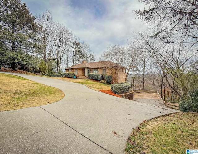 view of front of home featuring driveway, brick siding, a chimney, and a front yard