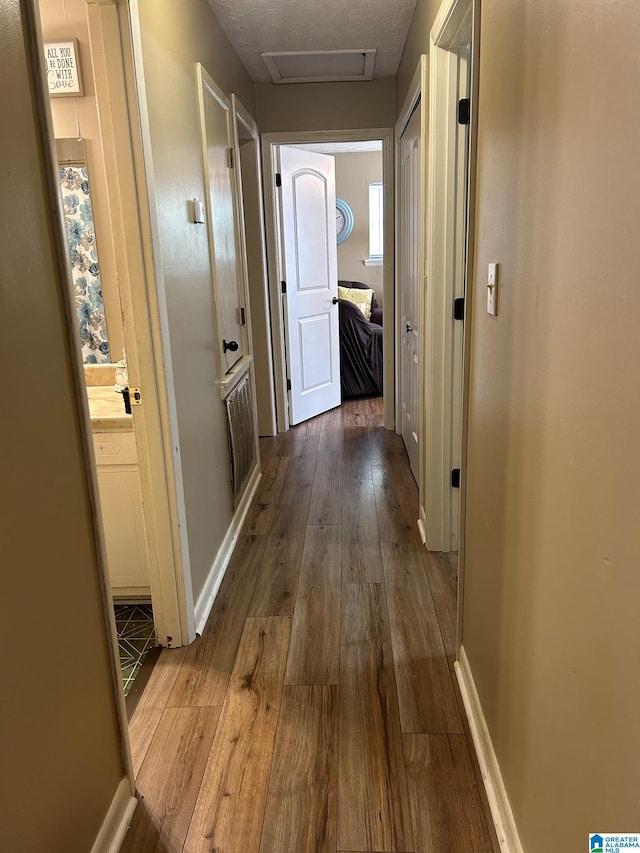 hallway featuring a textured ceiling, attic access, baseboards, and wood-type flooring