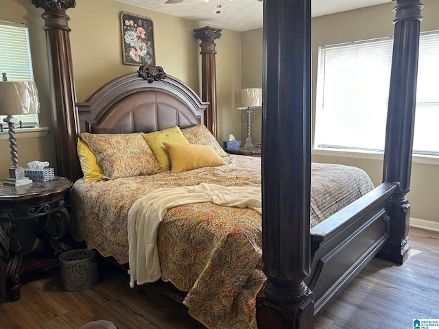 bedroom featuring ornate columns, a textured ceiling, baseboards, and wood finished floors