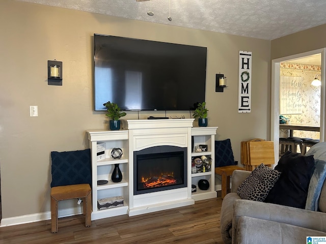 living area featuring a glass covered fireplace, wood finished floors, baseboards, and a textured ceiling