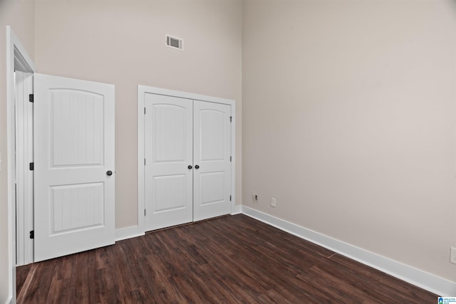 unfurnished bedroom featuring dark wood-type flooring, baseboards, visible vents, and a closet