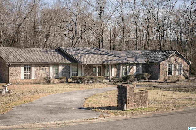 ranch-style home featuring a standing seam roof, brick siding, and metal roof