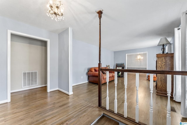 hallway with an inviting chandelier, baseboards, visible vents, and wood finished floors