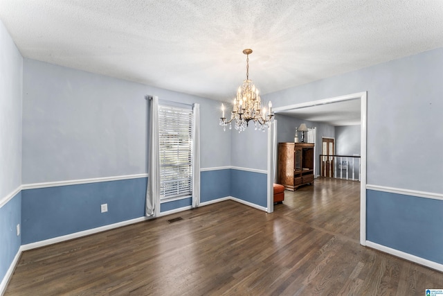 unfurnished room with visible vents, a textured ceiling, wood finished floors, a chandelier, and baseboards