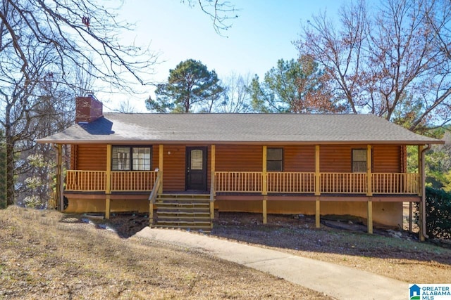 cabin featuring a shingled roof, covered porch, and a chimney