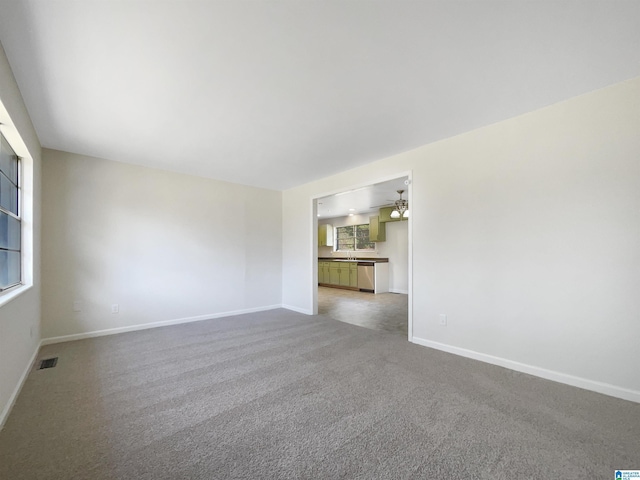 unfurnished room with carpet floors, visible vents, a sink, and baseboards