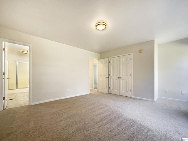 unfurnished bedroom featuring carpet floors, a closet, ensuite bath, and baseboards