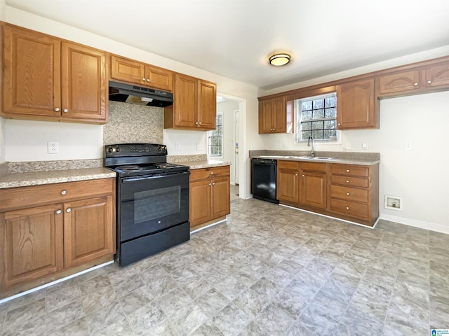 kitchen with brown cabinetry, a sink, under cabinet range hood, and black appliances