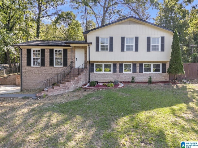 tri-level home featuring brick siding, a front lawn, and fence