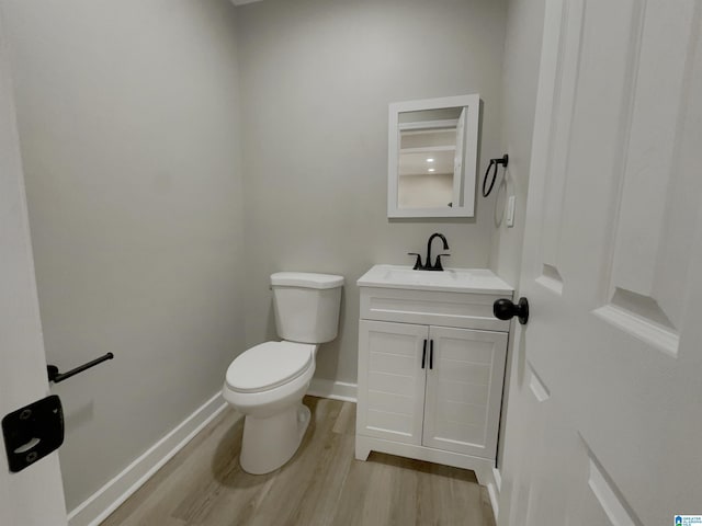 half bath featuring toilet, baseboards, wood finished floors, and vanity