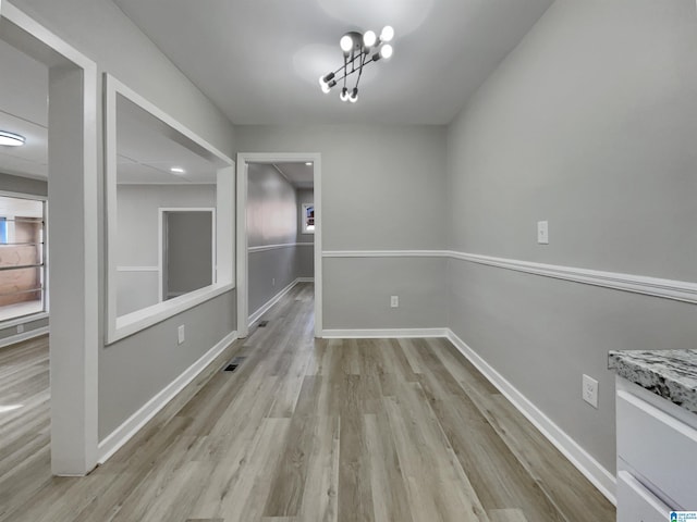 unfurnished dining area featuring light wood-type flooring, visible vents, baseboards, and an inviting chandelier