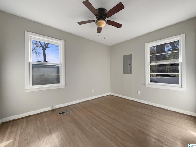 spare room featuring visible vents, dark wood-type flooring, a ceiling fan, electric panel, and baseboards