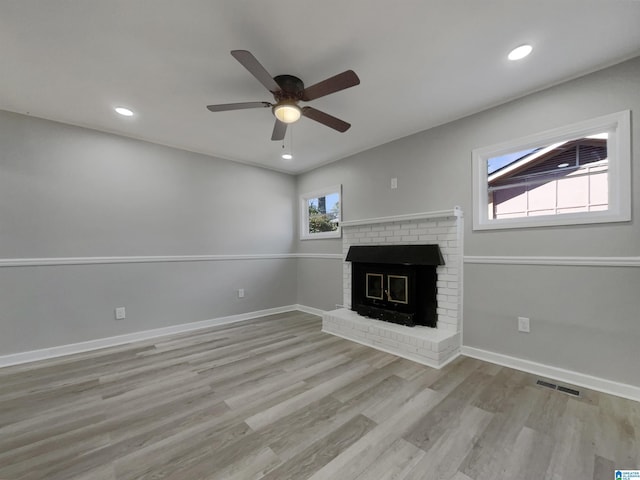 unfurnished living room featuring a brick fireplace, baseboards, visible vents, and wood finished floors