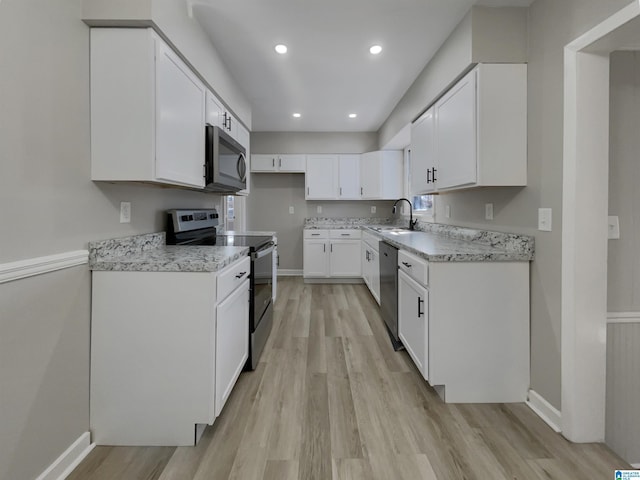 kitchen featuring light wood-type flooring, appliances with stainless steel finishes, white cabinets, and a sink