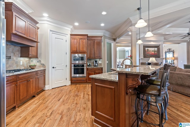 kitchen featuring a breakfast bar, hanging light fixtures, appliances with stainless steel finishes, light wood-style floors, and open floor plan