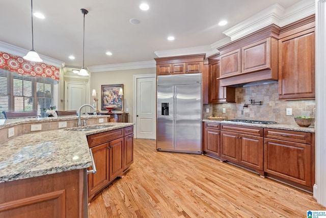 kitchen featuring crown molding, stainless steel appliances, hanging light fixtures, light wood-style floors, and a sink