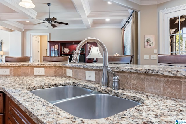 kitchen featuring light stone counters, coffered ceiling, a sink, and beamed ceiling