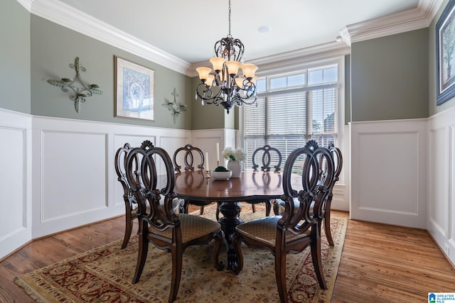 dining area featuring a chandelier, a decorative wall, crown molding, and wainscoting