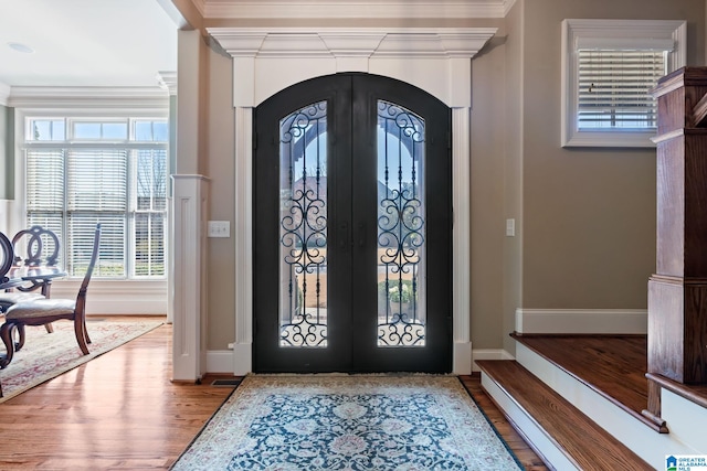 foyer with arched walkways, french doors, wood finished floors, and ornamental molding