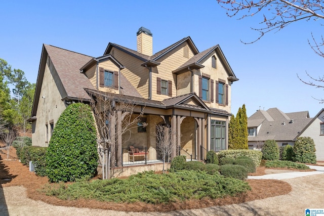 view of front of house with covered porch, a shingled roof, a chimney, and stucco siding