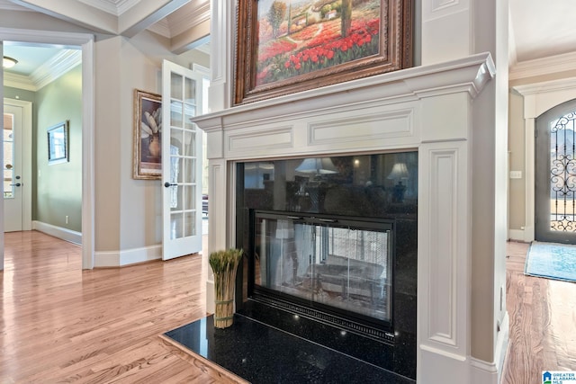 interior details with wood finished floors, ornamental molding, a glass covered fireplace, and baseboards