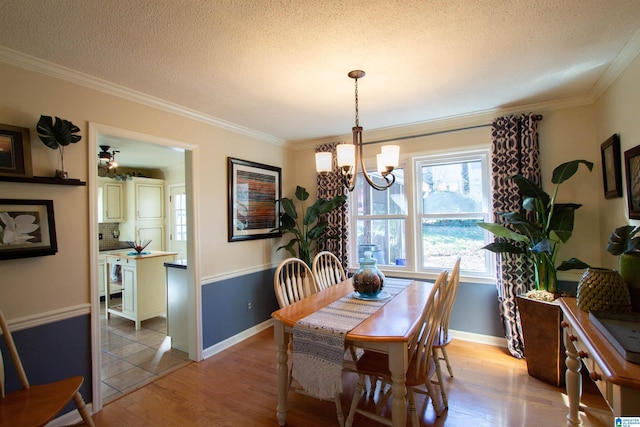 dining area with a textured ceiling, ornamental molding, and light wood-style floors