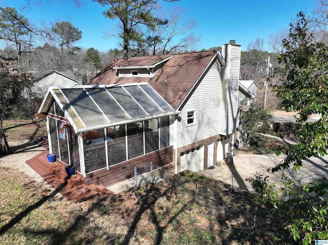 back of property with an attached garage, a sunroom, driveway, roof with shingles, and a chimney