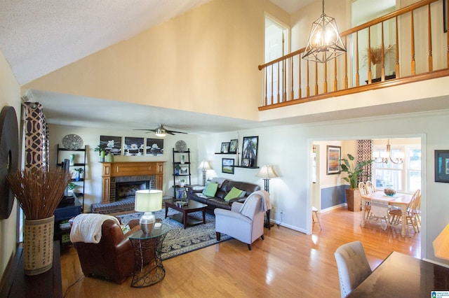 living area featuring a fireplace, wood finished floors, high vaulted ceiling, baseboards, and ceiling fan with notable chandelier