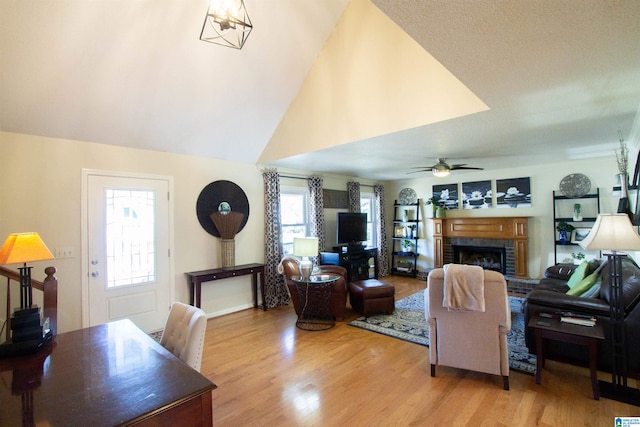 living room featuring a ceiling fan, lofted ceiling, a fireplace, and light wood finished floors