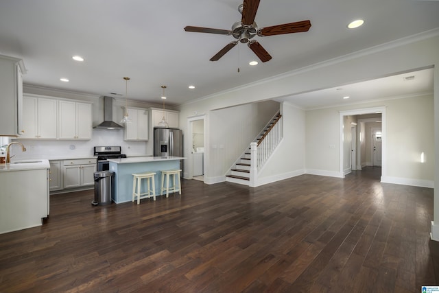 kitchen with dark wood-style flooring, light countertops, wall chimney range hood, appliances with stainless steel finishes, and a center island