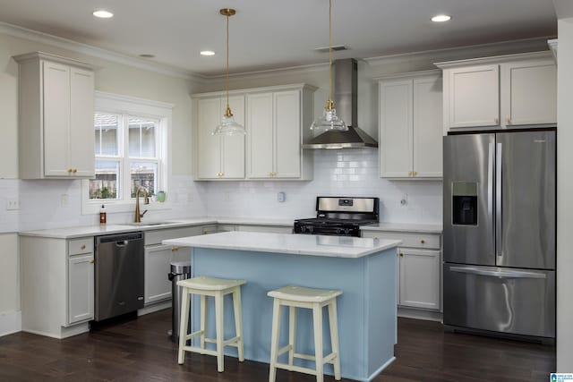 kitchen featuring wall chimney exhaust hood, appliances with stainless steel finishes, a center island, light countertops, and crown molding