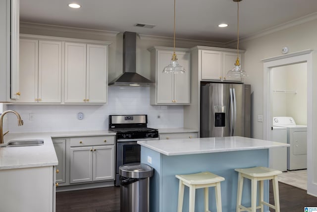 kitchen featuring washing machine and dryer, a sink, visible vents, appliances with stainless steel finishes, and wall chimney exhaust hood