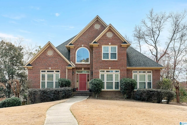 traditional home featuring brick siding, a front lawn, and roof with shingles