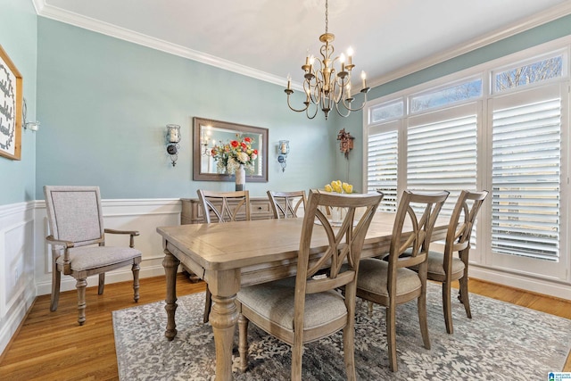 dining space featuring a decorative wall, ornamental molding, light wood-style floors, wainscoting, and a chandelier