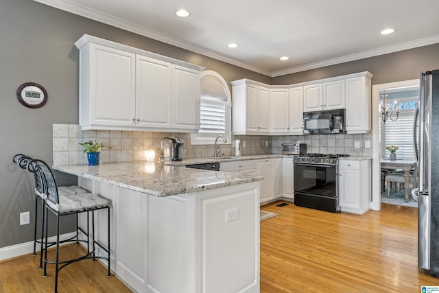 kitchen featuring black appliances, a peninsula, white cabinetry, and light wood-style floors