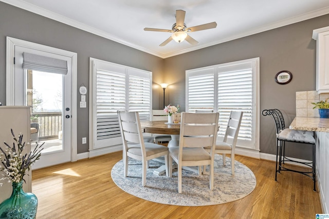 dining room featuring light wood-type flooring, crown molding, baseboards, and ceiling fan