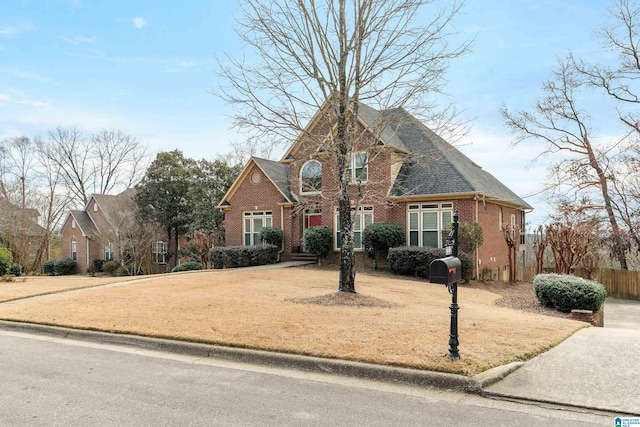 traditional-style home featuring brick siding, roof with shingles, a front yard, and fence