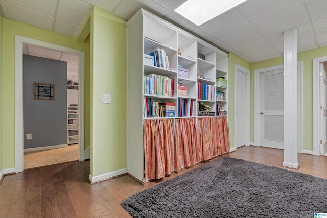 hallway with a drop ceiling, wood finished floors, and baseboards