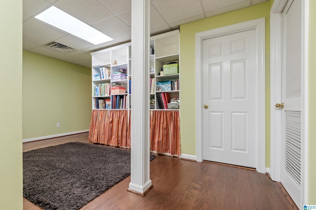 interior space with a paneled ceiling, baseboards, visible vents, and wood finished floors