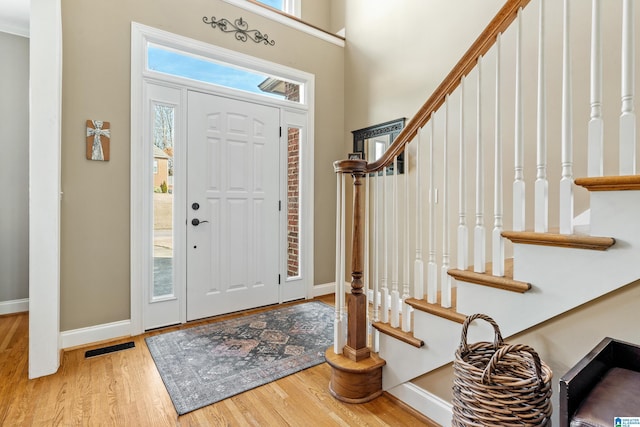 entrance foyer featuring visible vents, baseboards, a towering ceiling, wood finished floors, and stairs