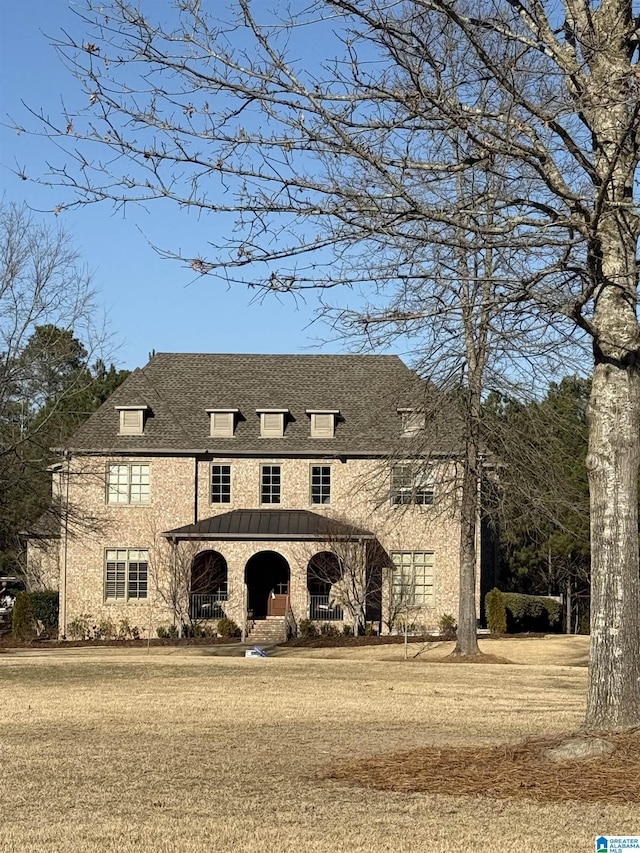 french country style house with covered porch, a shingled roof, and a front yard