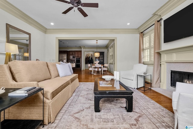 living area with recessed lighting, a fireplace, wood finished floors, and crown molding